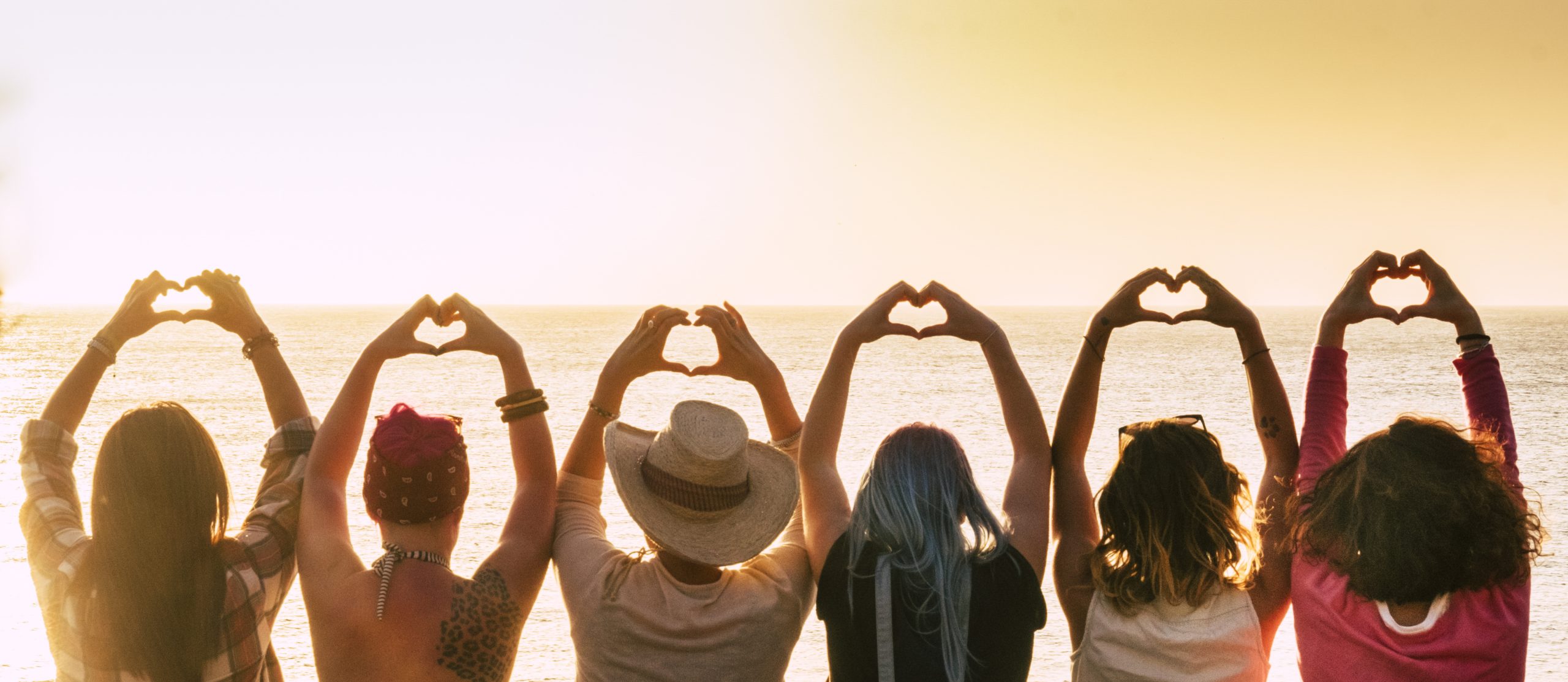 Group of diversity alternative young woman enjoying the sunset at the sea doing hearth symbol with hands - people enjoying friendly lifestyle - vacation in friendship concept for females