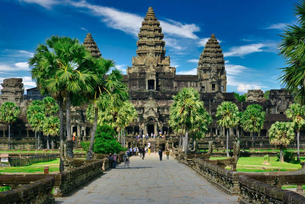 Temple d'Angkor Wat entouré de palmiers, avec des visiteurs empruntant l'allée principale menant à l'entrée du monument. Siem Reap, Cambodge.